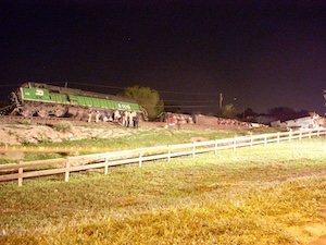 Derailed train engine with a few emergency workers.