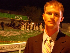 Investigator Trevor Materasso in front of a derailed train engine and emergency workers.
