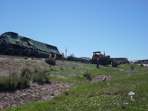 A derailed train with workers and bulldozer at the scene.