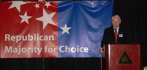 Hank Brown speaking at a lectern in front of a Republican Majority for Choice sign.