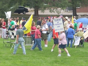 A crowd gathers at a park as a woman holds a sign reading Chains of Tyranny are Rattling.