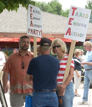 A man and woman hold signs reading Taxed Enough Already as they speak to another man.