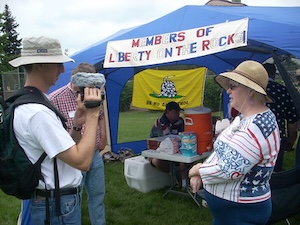 Ari Armstrong with a video camera interviewing a woman outside a tent with a sign Members of Liberty On the Rocks.