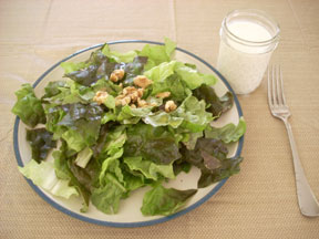 A leaf salad with walnuts, along with a cup of milk.