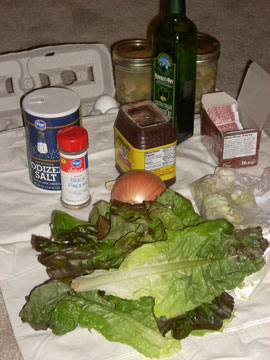 A carton with one egg, salt, pepper, pints of soup, a bottle of oil, powdered chocolate, tea bags, and onion, and some lettuce leaves.