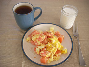 Breakfast with scrambled eggs and tomatoes, tea, and milk.