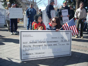 A woman holding an American flag kneels beside her child as she holds a large check reading Thirty Thousand Dollars to the United States Government.