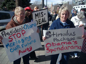 Two women hold signs reading President Obama Stop Mortgaging Our Future Away and Stimulus Package equals Obama's Spendorama.