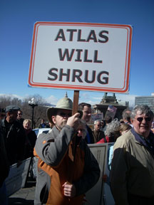 A man holds a sign reading Atlas Will Shrug.