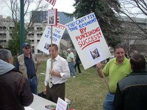 Anthony Gillis holds a sign reading You Can't Fix the Economy by Punishing Success.