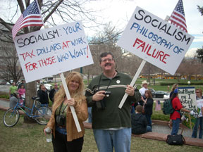 A woman holds a sign that reads Socialism Your Tax Dollars at Work for Those Who Won't, and a man holds a sign that reads Socialism Philosophy of Failure.