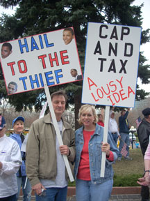 A man holds a sign reading Hail to the Thief, a woman holds a sign reading Cap and Tax a Lousy Idea.