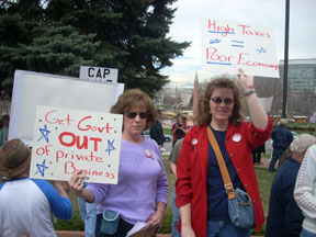 Two women hold signs reading Get Government Out of Private Business and High Taxes equal Poor Economy.