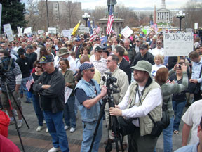 A man holds a video camera in front of a crowd.