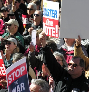 A man in a crowd holds a sign reading One Teamster One Vote.