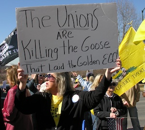 A woman holds a sign reading the unions are killing the goose that laid the golden egg.