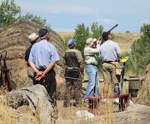Someone holds a shotgun while several others observe from behind.