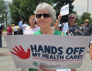 A woman holds a sign reading Hands Off My Health Care.