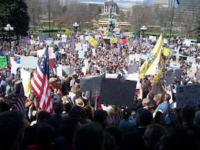 A large crowd waiving flags and signs gathers on the front steps of the Colorado capitol.