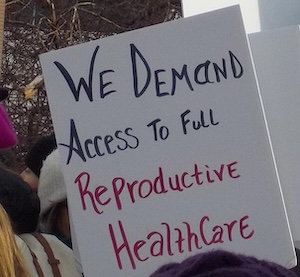 A sign reads We demand access to full reproductive healthcare.