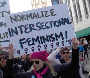 A woman holds a sign reading normalize intersectional feminism.