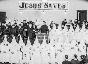 Beneath a large sign saying Jesus Saves, the pastor of a Colorado church surrounds himself with hooded members of the Ku Klux Klan.