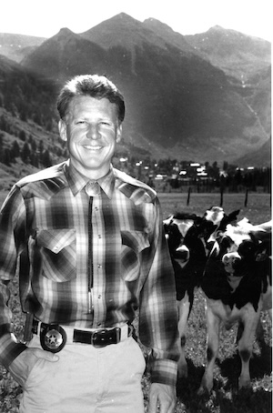 Bill Masters, wearing a plaid shirt, posing in front of some cows.